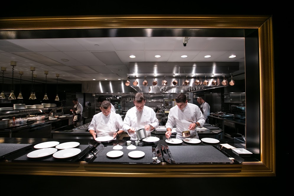 Three chefs plating meals at the kitchen window