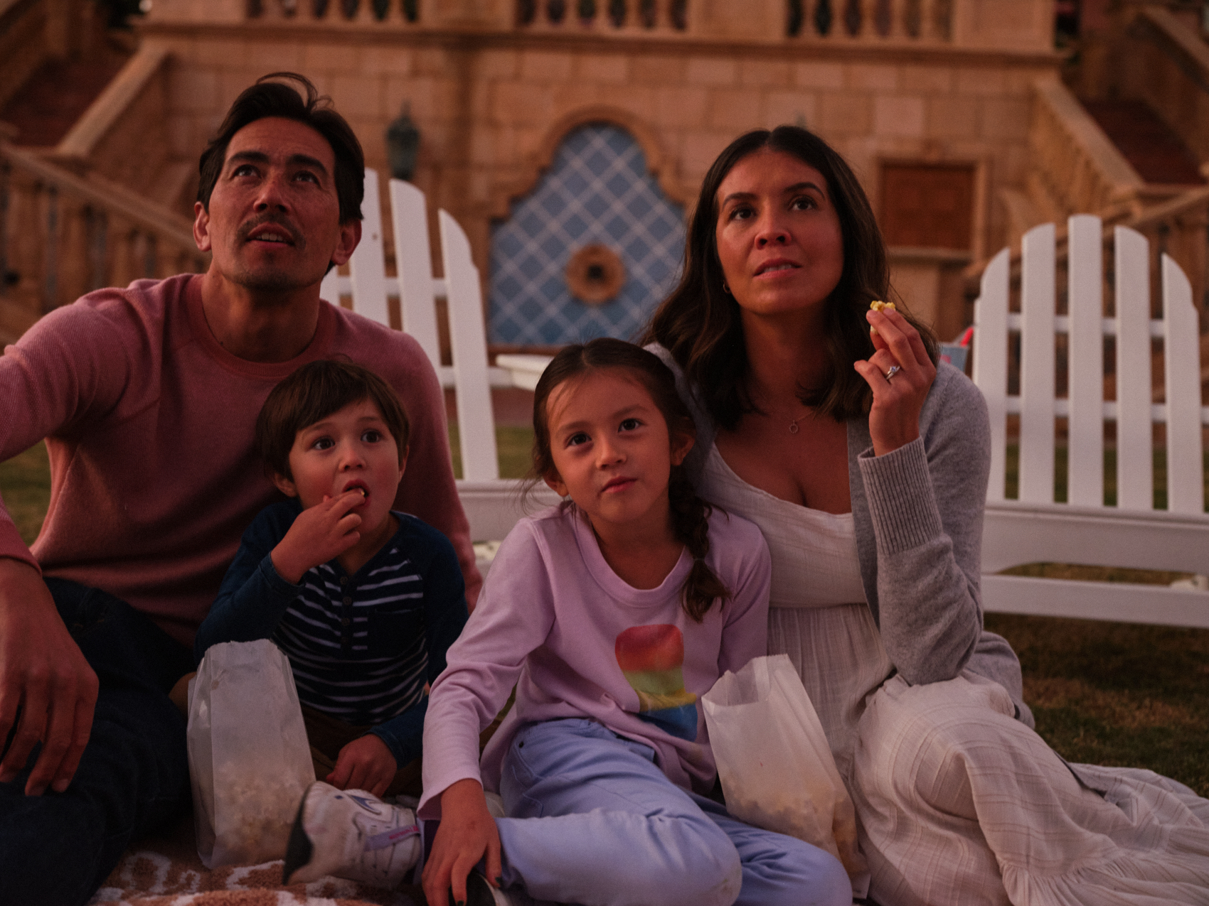 Family eating popcorn in grass outside while watching a movie